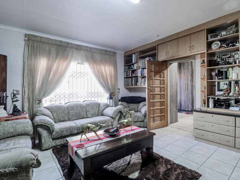 A living room featuring extensive built-in wooden cabinetry, tiled flooring, and a security gate over the window, providing functional storage and access to adjacent rooms.