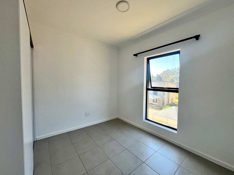 A clean, empty bedroom featuring neutral tiled flooring, a built-in cupboard, and a modern aluminium window frame.