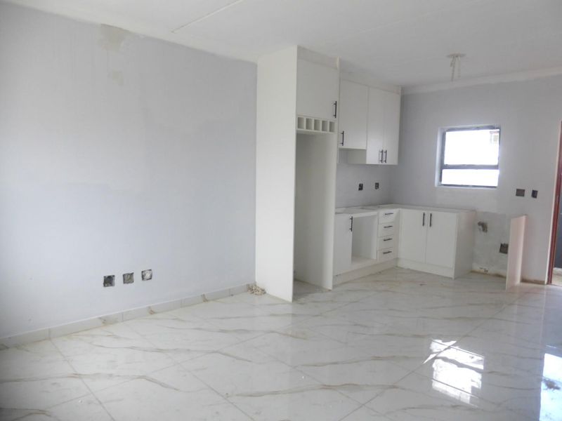 An open-plan living and kitchen area featuring white cabinetry, marble-look floor tiles, and unfinished wall surfaces awaiting final touches.
