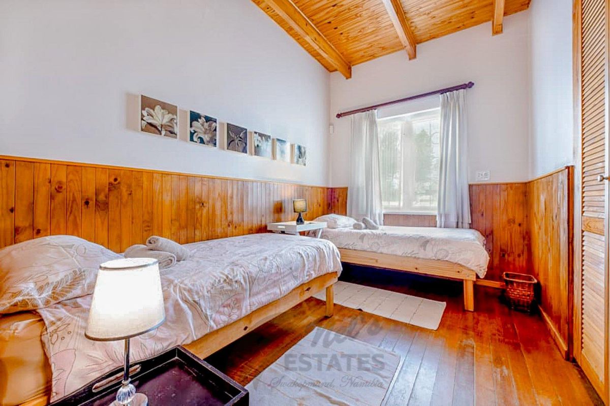 A bedroom featuring timber wall paneling, exposed wooden ceiling beams, and polished wooden flooring, creating a rustic aesthetic.