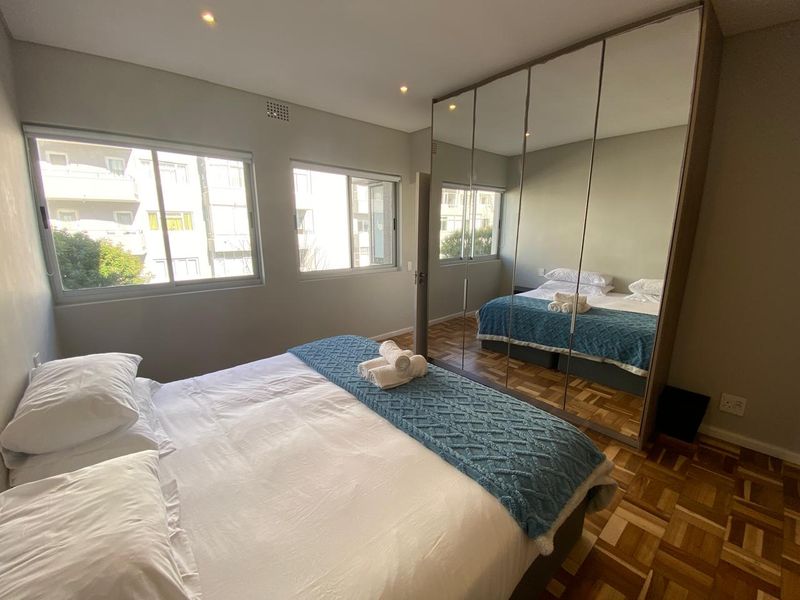 A well-maintained bedroom featuring classic parquet flooring, recessed downlighting, and a large floor-to-ceiling mirrored built-in wardrobe.