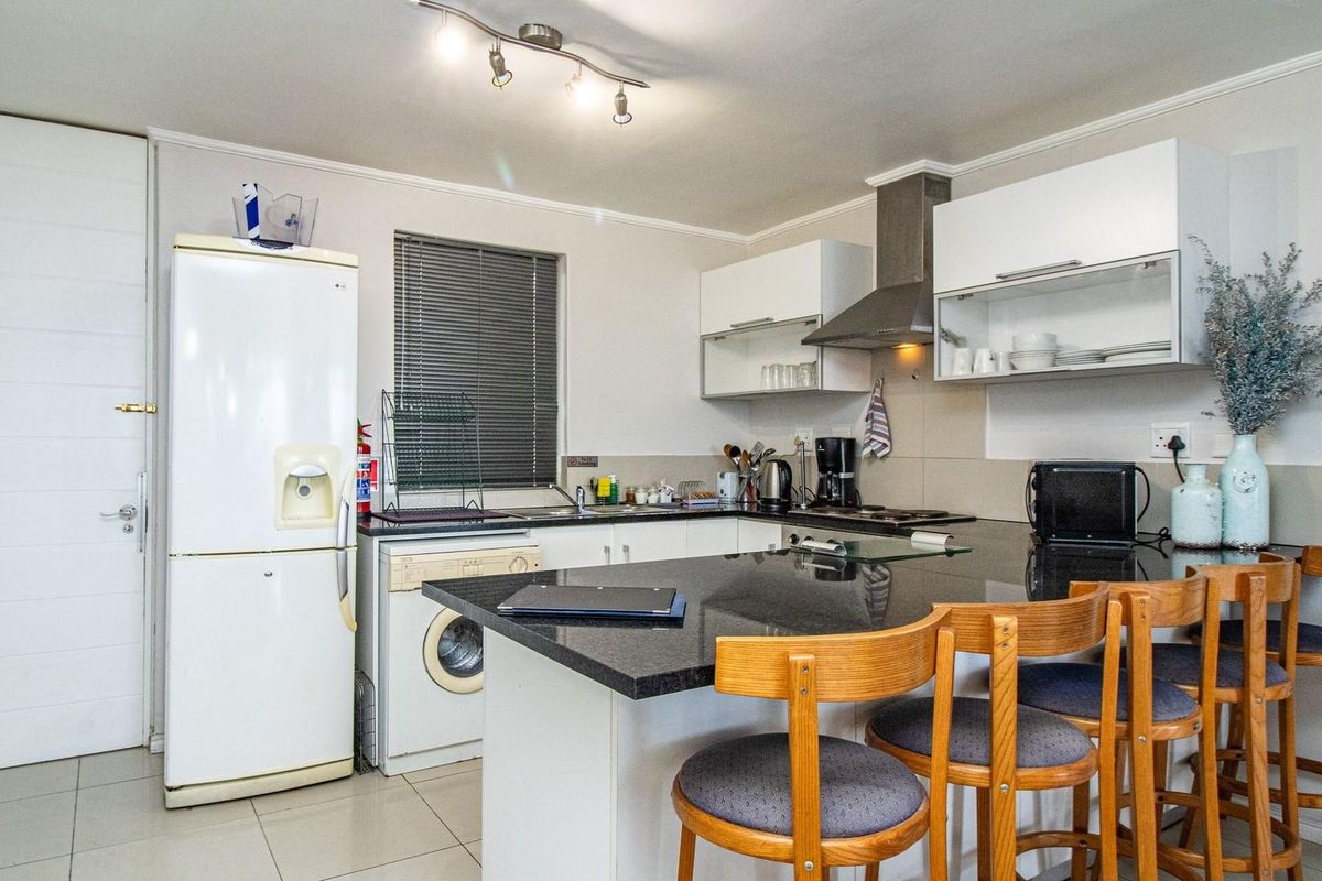A functional kitchen featuring dark granite countertops, white cabinetry, a built-in hob with extractor fan, and integrated laundry plumbing.
