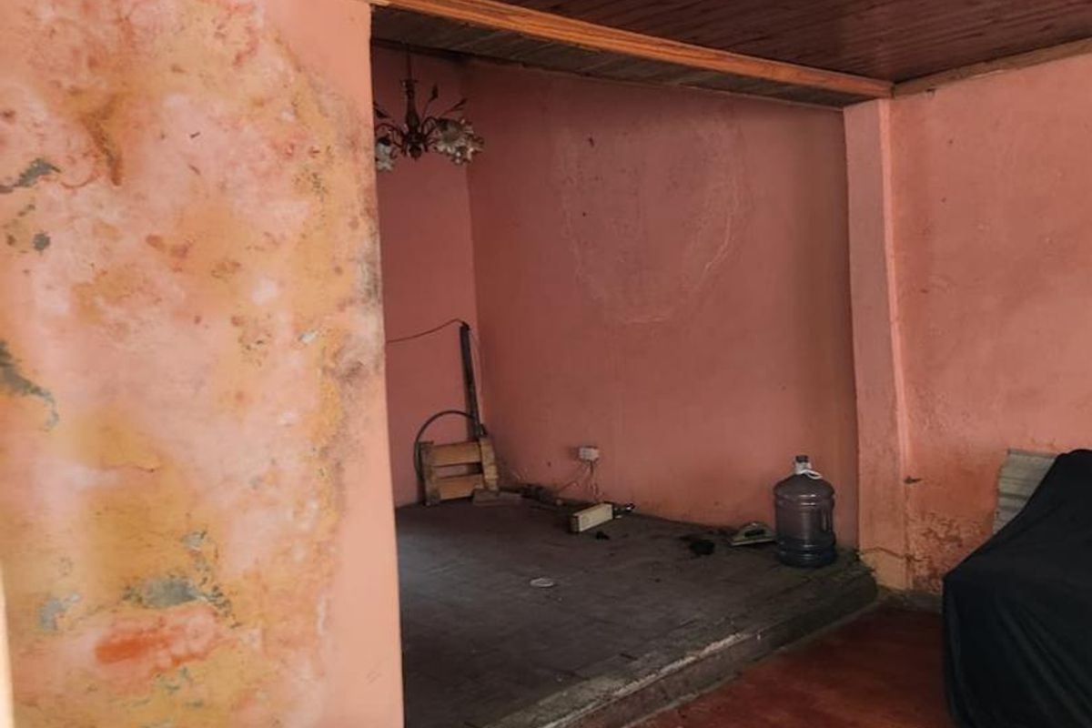 An interior living space featuring timber ceiling panels and laminate flooring, currently requiring significant wall repairs and cosmetic refurbishment.
