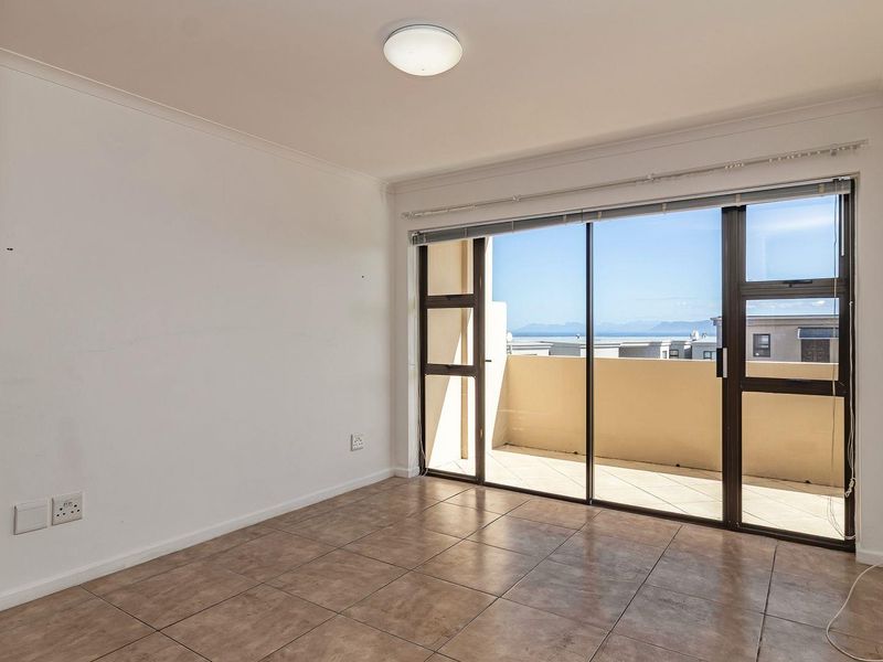 An empty bedroom featuring tiled flooring, a built-in cupboard, and a sliding glass door providing access to a balcony with scenic views.