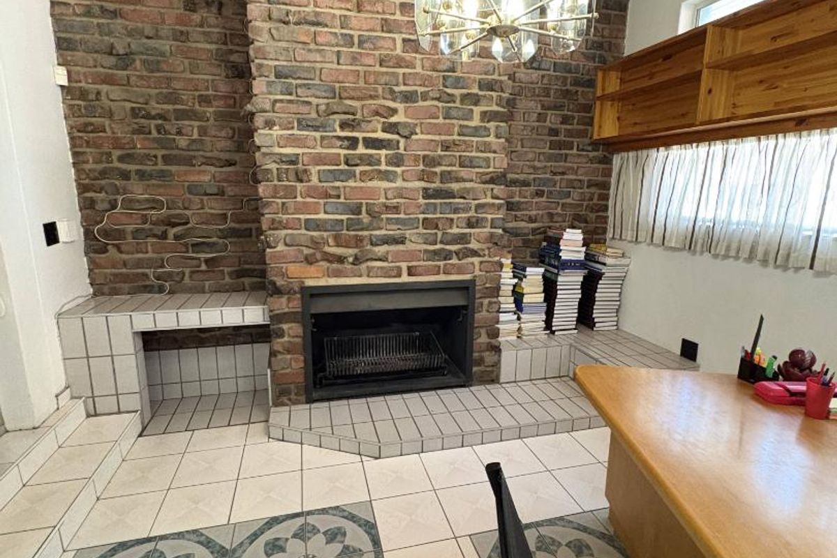 Living room featuring a prominent brick fireplace with a tiled hearth, timber-clad ceiling, and patterned tile flooring.
