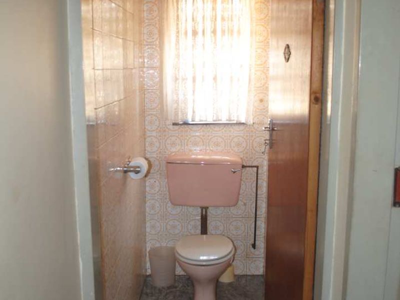 A compact, dated bathroom featuring original pink sanitaryware and patterned ceramic wall tiles, offering potential for a modern renovation.