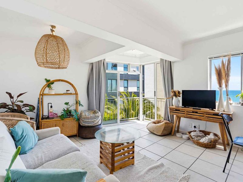 Bright and airy living room featuring tiled flooring and large sliding glass doors that open onto a balcony with ocean views.