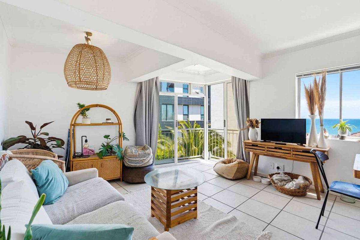 Bright and airy living room featuring tiled flooring and large sliding glass doors that open onto a balcony with ocean views.