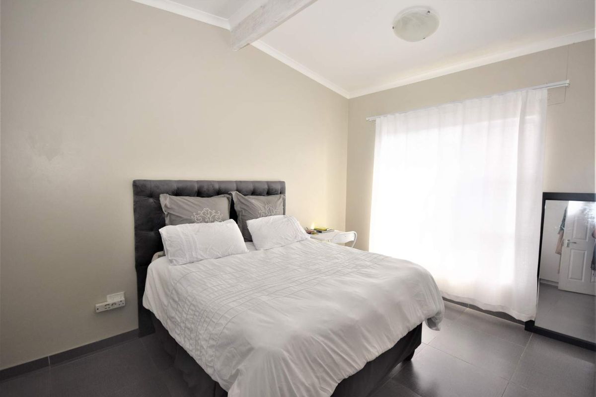 A well-lit bedroom featuring neutral wall tones, tiled flooring, and a large window with sheer curtains, providing a comfortable and functional living space.