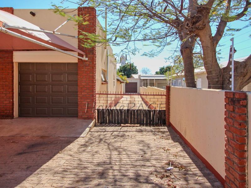 Front exterior view featuring a paved driveway, garage access, brick boundary wall with electric fencing, and a metal gate.