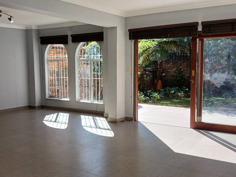 Spacious, light-filled living area featuring tiled floors, arched windows with security bars, and large sliding doors opening onto a private garden patio.