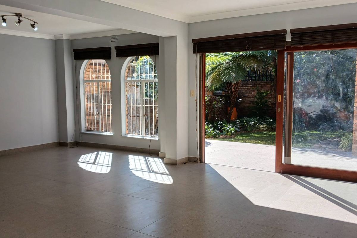 Spacious, light-filled living area featuring tiled floors, arched windows with security bars, and large sliding doors opening onto a private garden patio.