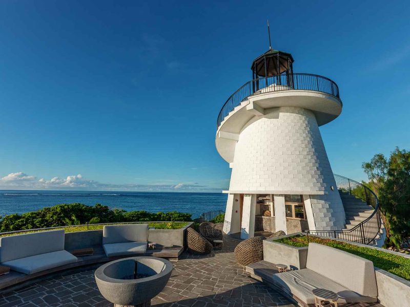 A unique outdoor entertainment area featuring a lighthouse-style structure, stone paving, built-in concrete seating, and panoramic ocean views.