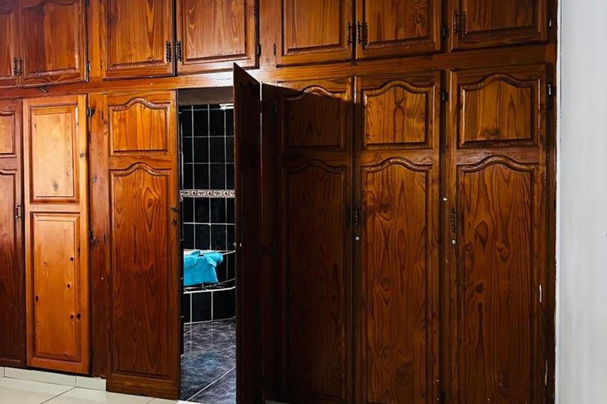 Bedroom featuring extensive floor-to-ceiling wooden built-in cupboards with integrated access to an en-suite bathroom and tiled flooring.
