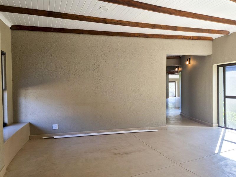 Spacious living area featuring exposed timber ceiling beams, neutral textured walls, and tiled flooring, leading into a connecting hallway with warm accent lighting.