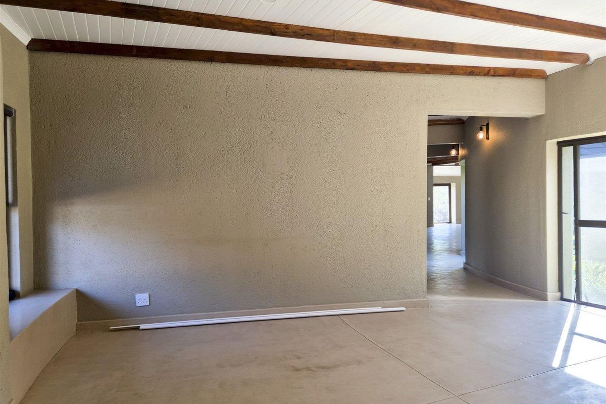 Spacious living area featuring exposed timber ceiling beams, neutral textured walls, and tiled flooring, leading into a connecting hallway with warm accent lighting.