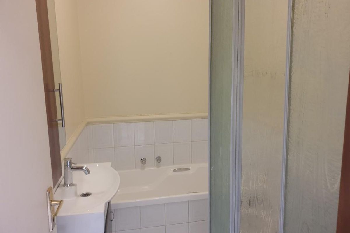 A functional bathroom featuring a built-in bathtub, wall-mounted basin with chrome fixtures, and a separate shower enclosure with tiled surrounds.