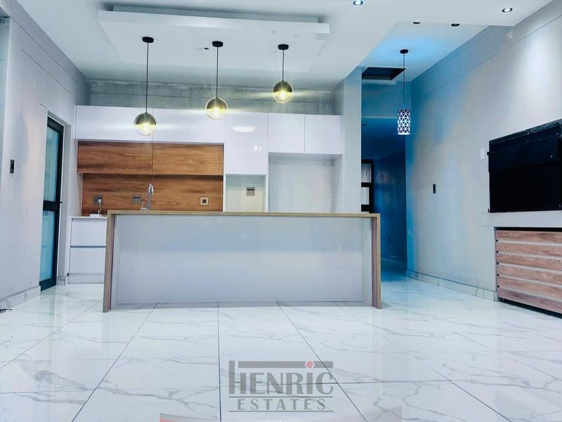 Modern open-plan living area featuring a sleek kitchen with built-in cabinetry, a central island, and polished tiled flooring throughout.