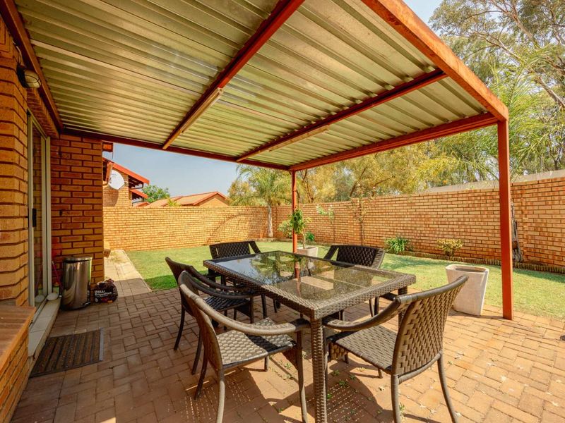A covered outdoor patio area featuring a corrugated metal roof, brick boundary walls, and paved flooring, providing a functional space for outdoor dining.
