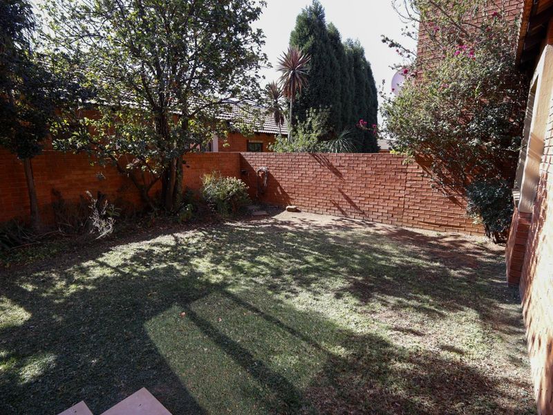 A private rear garden area featuring a lawn, mature trees, and a solid brick boundary wall.