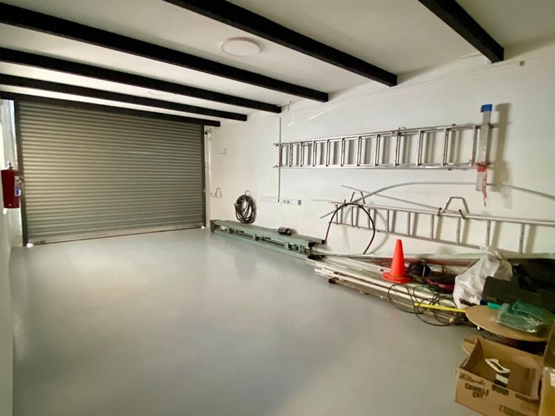 A spacious, clean garage featuring a roller shutter door, exposed ceiling beams, and a durable epoxy floor finish.