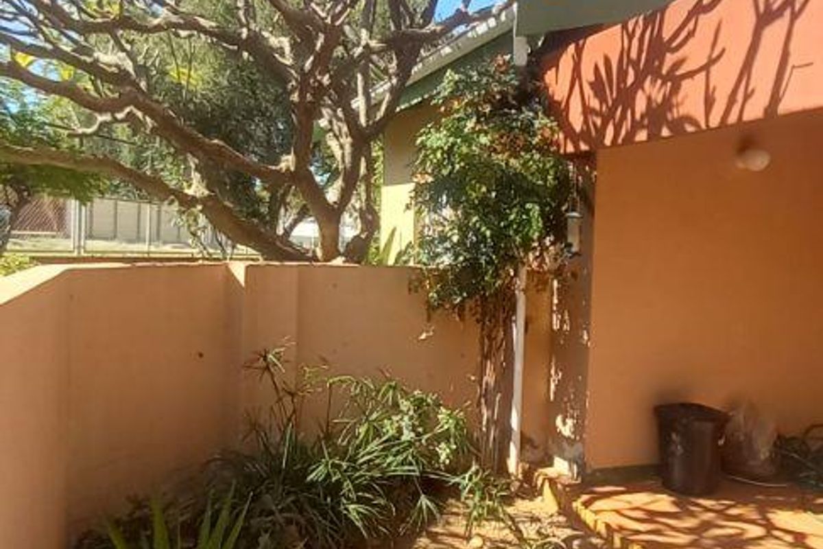 A rear garden area featuring a paved patio section, boundary walls, and established trees, providing a private outdoor space for the townhouse.