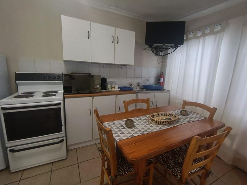 Compact open-plan kitchen and dining area featuring white cabinetry, tiled flooring, and a functional electric stove.