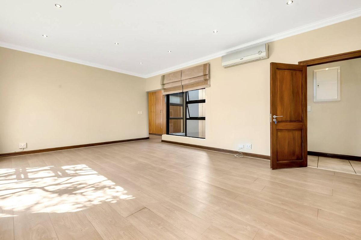 A spacious, light-filled bedroom featuring modern laminate flooring, built-in cabinetry, recessed lighting, and a wall-mounted air conditioning unit.