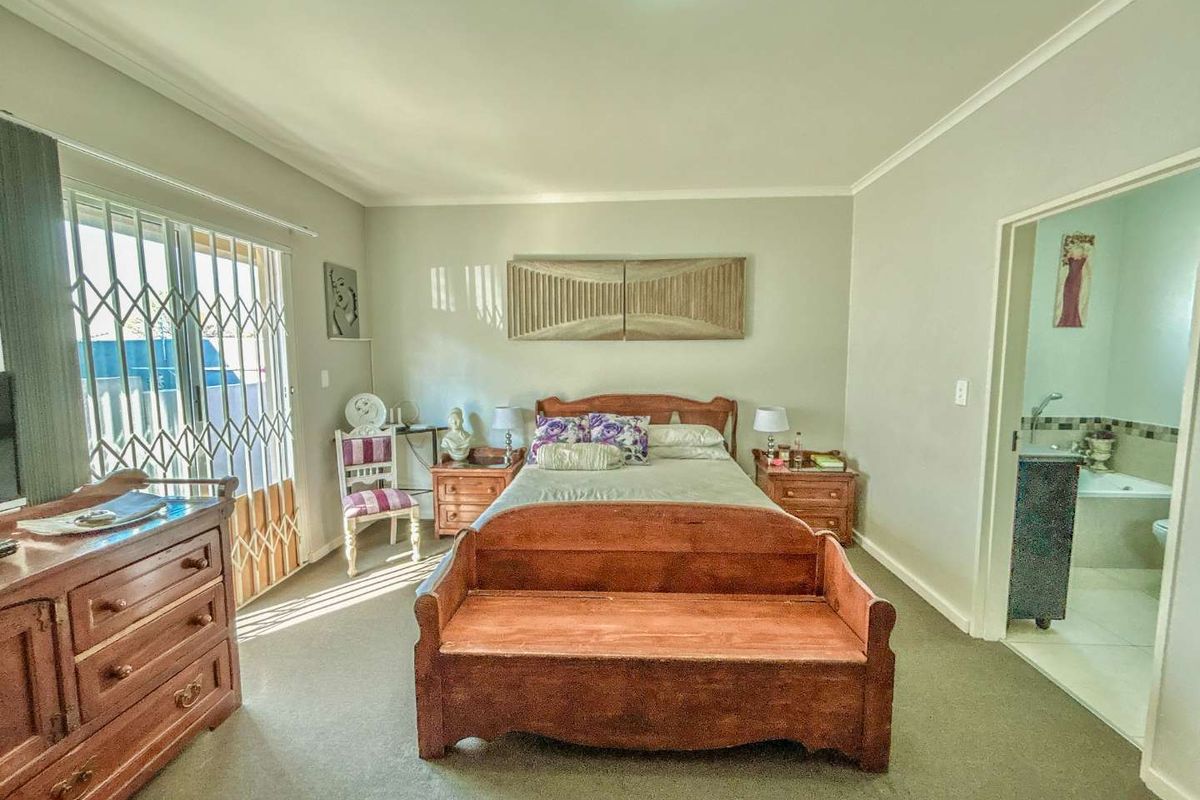 Spacious bedroom featuring neutral walls, carpeted flooring, and an en-suite bathroom, with direct access to an outdoor area through a security gate.