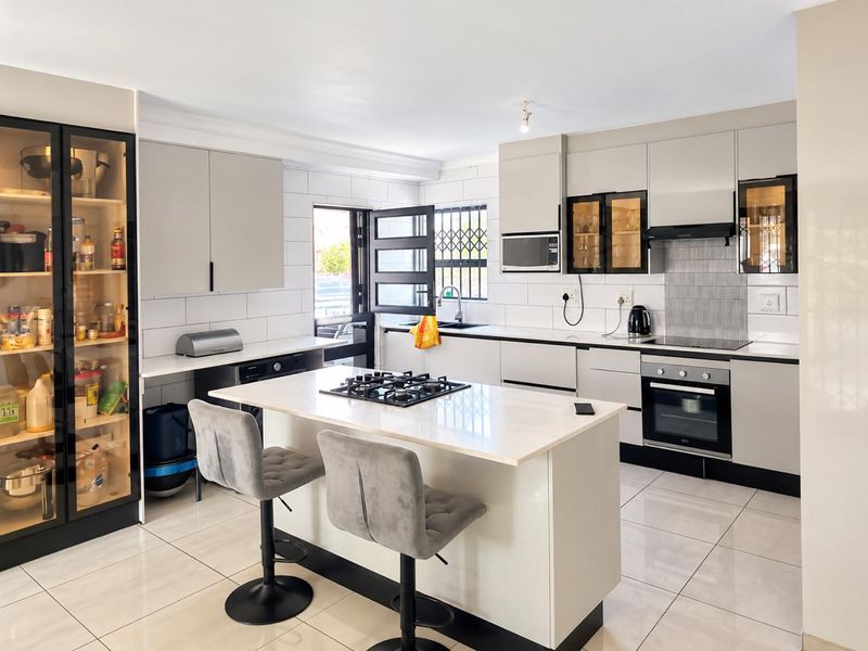 Modern kitchen featuring a central island with gas hob, built-in oven, sleek cabinetry, tiled flooring, and a functional layout with integrated appliances.
