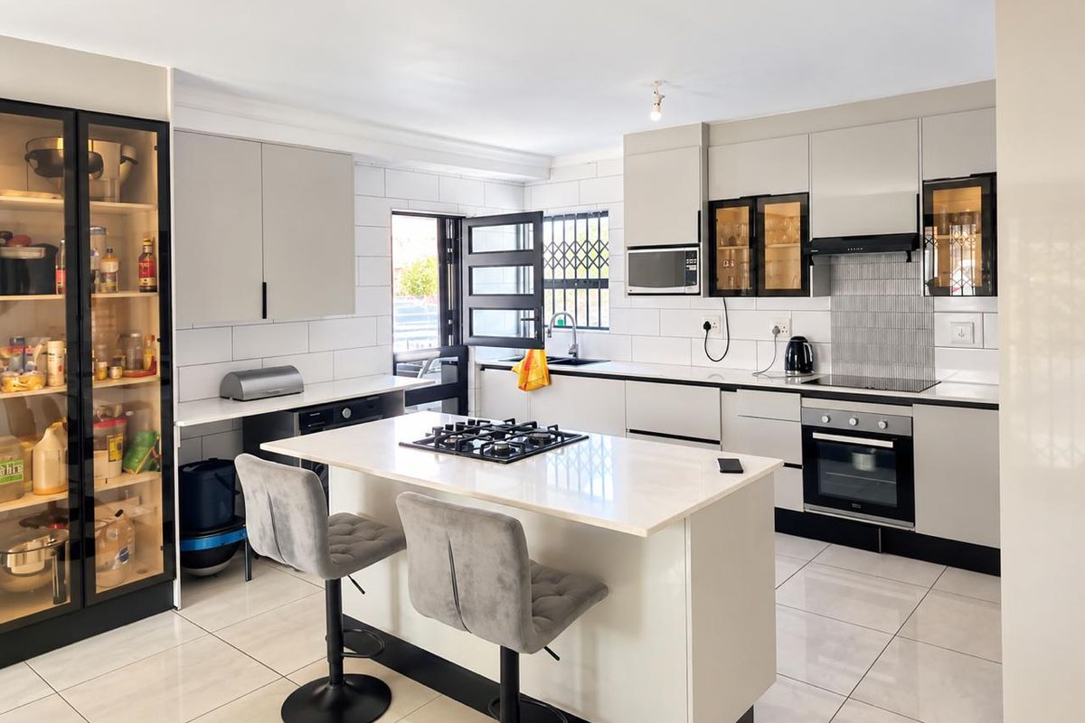Modern kitchen featuring a central island with gas hob, built-in oven, sleek cabinetry, tiled flooring, and a functional layout with integrated appliances.