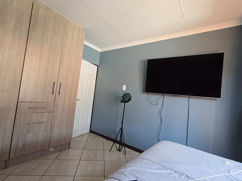 A bedroom featuring light wood-grain built-in wardrobes, tiled flooring, and blue accent wall with wall-mounted television.