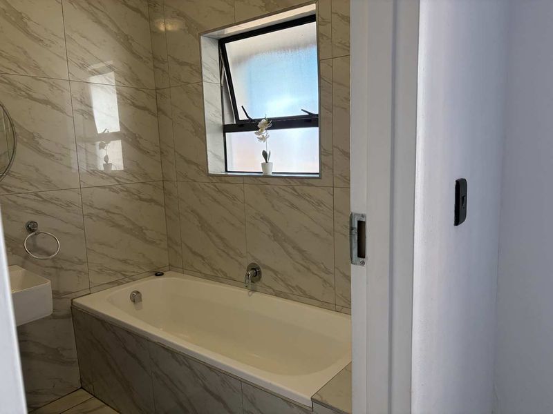 A clean, modern bathroom featuring marble-look wall tiling, a built-in bathtub, and a wall-mounted basin with a top-hung window for natural light.