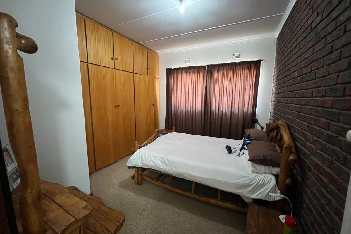 A bedroom featuring built-in wooden cupboards and a distinctive exposed brick feature wall.