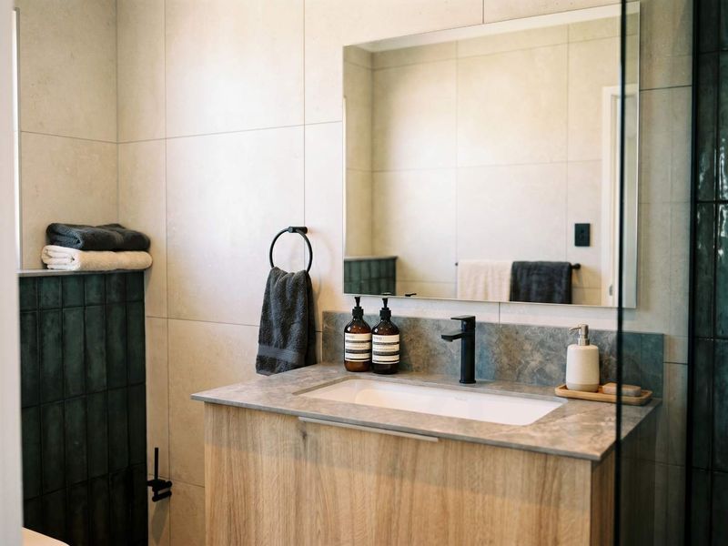 Modern bathroom featuring a wood-finish vanity cabinet, stone countertop with undermount sink, black fixtures, and neutral wall tiling.