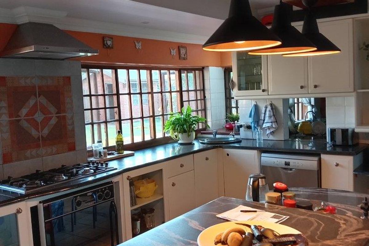 A well-appointed kitchen featuring a central island with stone countertop, built-in gas hob, stainless steel extractor fan, and ample cabinetry.