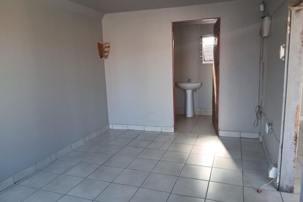 An empty room with tiled flooring, featuring an adjacent small bathroom area with a pedestal basin and window.