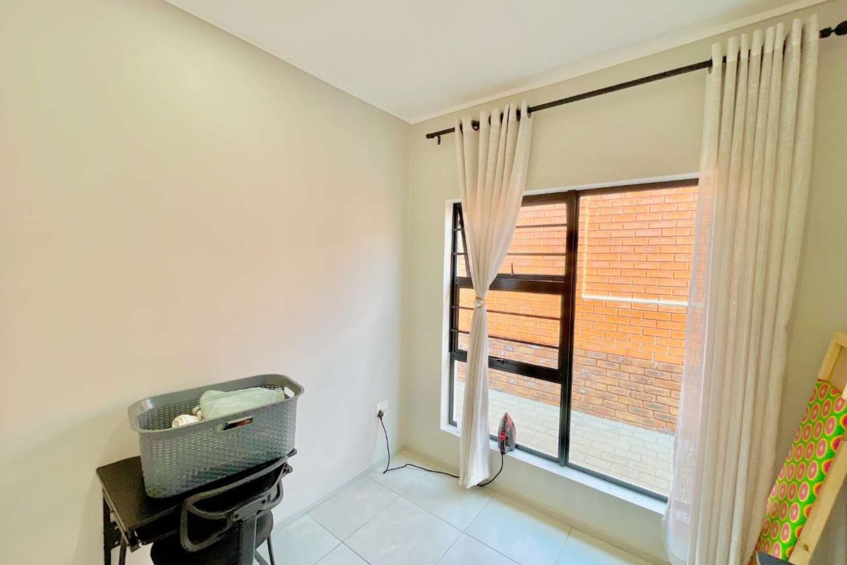 A bright bedroom featuring tiled flooring, a large window with security bars, and neutral wall finishes.