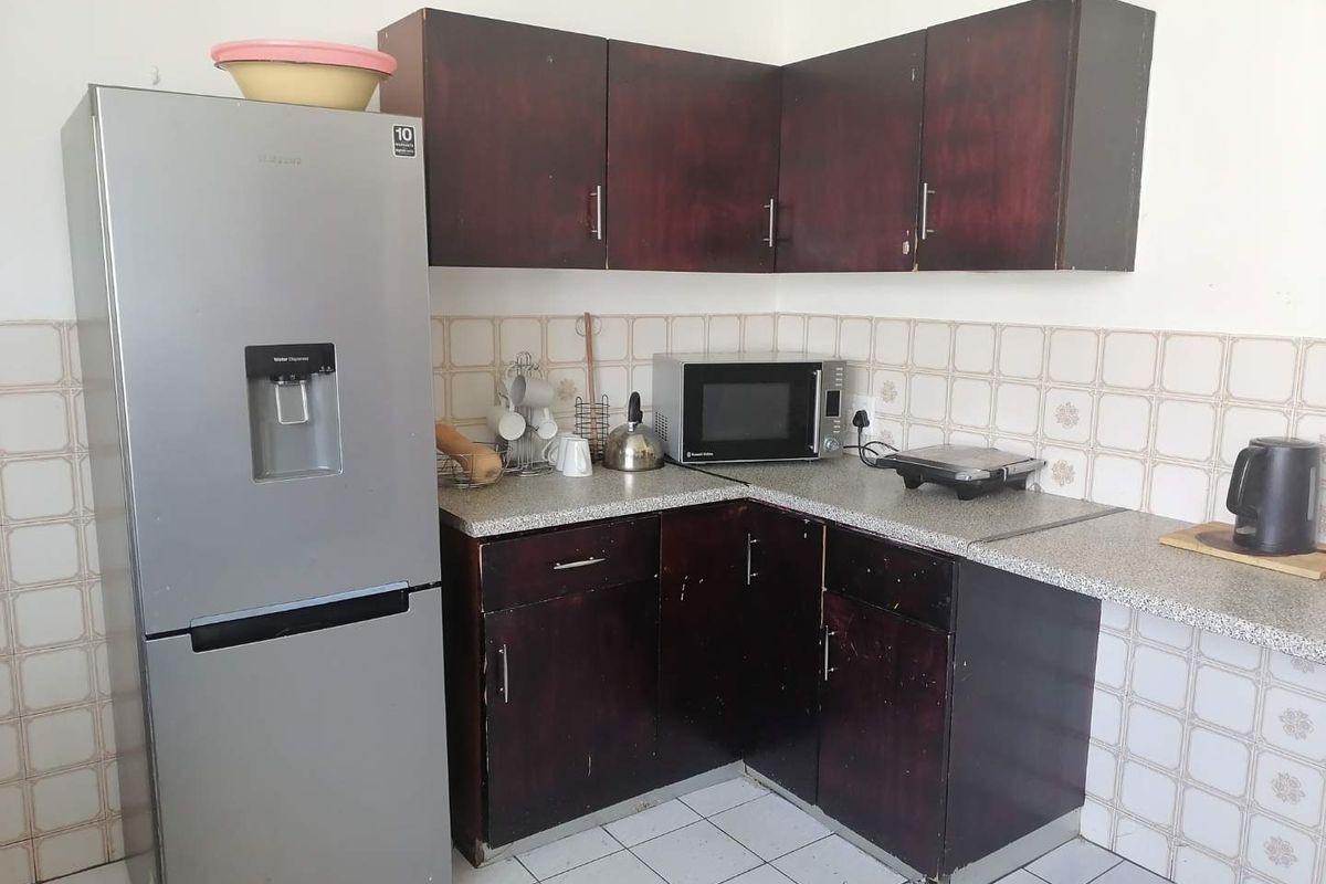 A compact kitchen featuring dark wood-finish cabinetry, laminate countertops, and neutral ceramic wall and floor tiles.