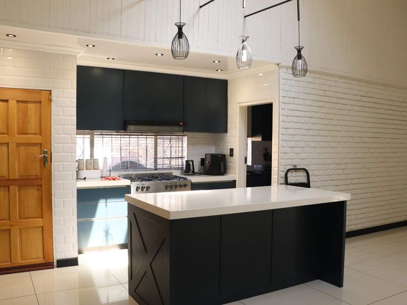 Modern kitchen featuring dark cabinetry, a central island with quartz countertops, gas stove, and stylish pendant lighting against a white exposed brick wall.