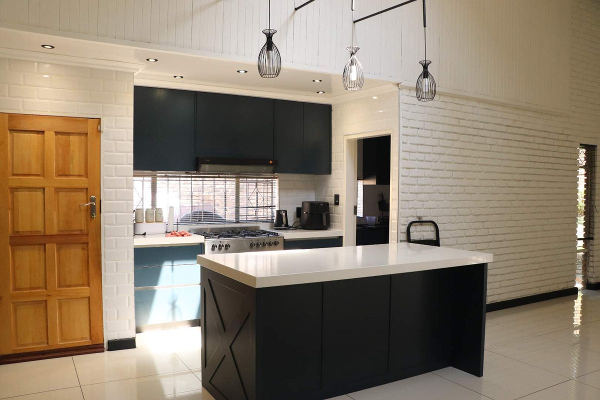 Modern kitchen featuring dark cabinetry, a central island with quartz countertops, gas stove, and stylish pendant lighting against a white exposed brick wall.