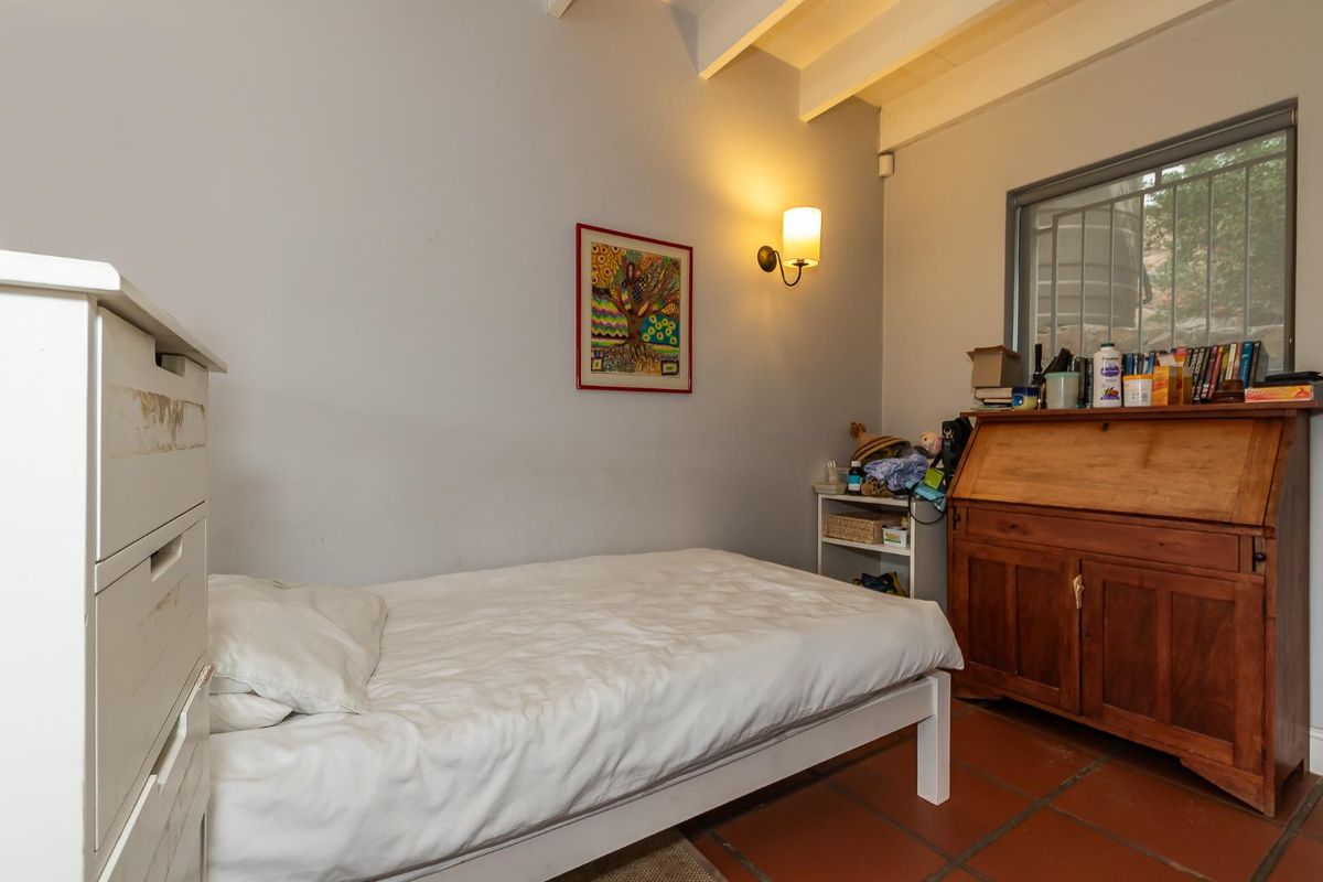 A bedroom featuring terracotta floor tiles, exposed ceiling beams, and a wall-mounted light fixture.