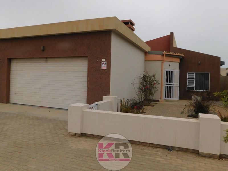 Front exterior view of a modern house featuring a single garage, paved driveway, and a low boundary wall with a security gate.