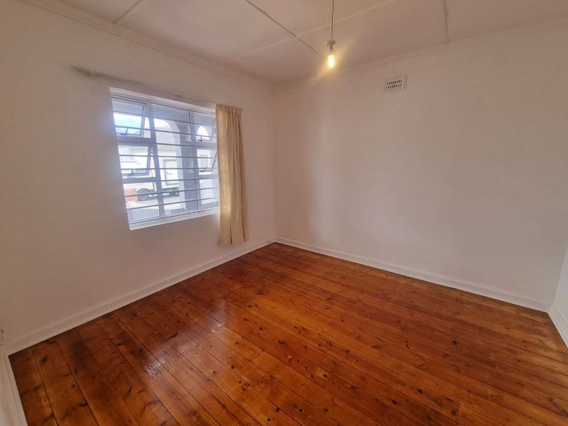 A bright, empty bedroom featuring polished timber flooring, a window with security bars, and a ceiling vent.