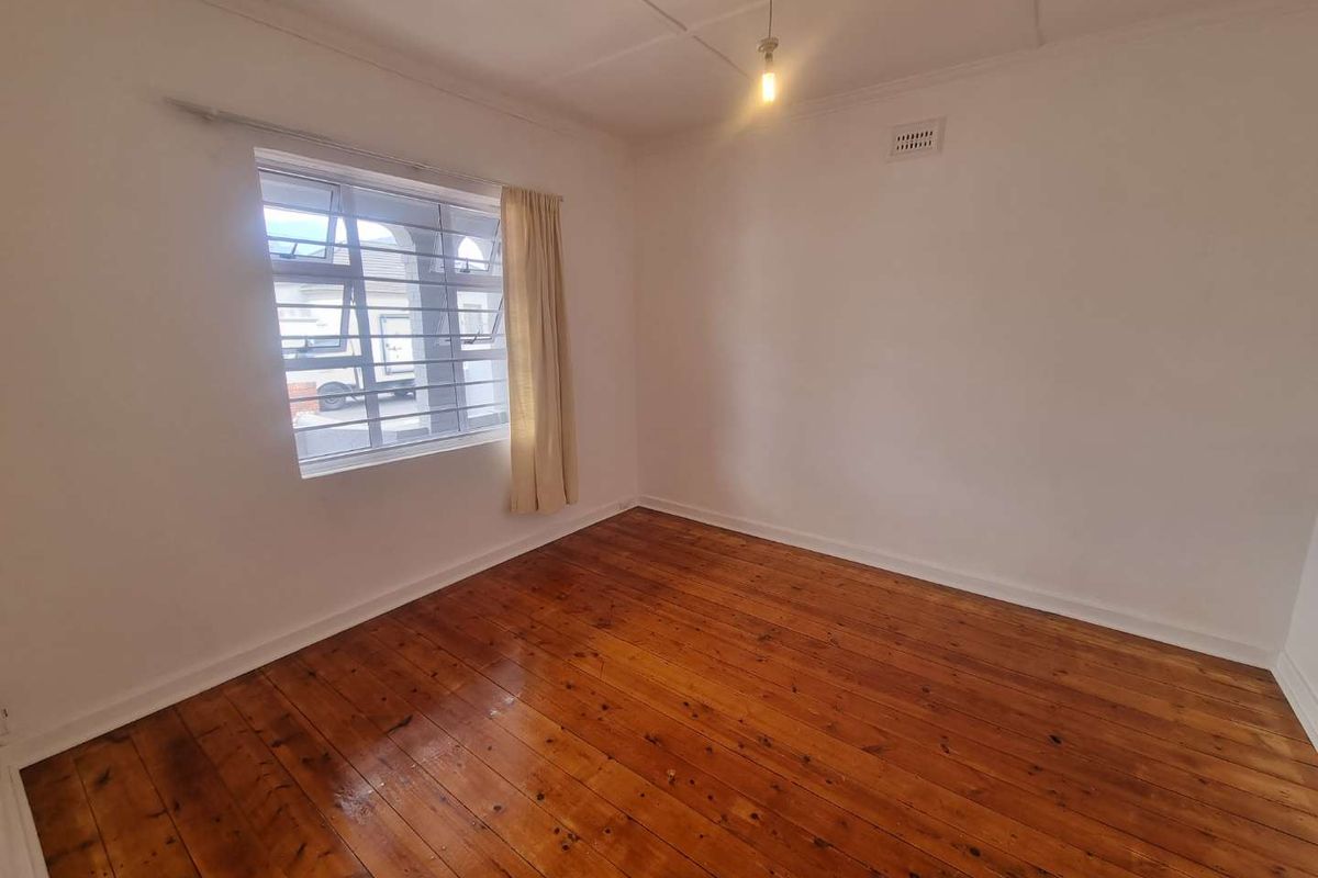 A bright, empty bedroom featuring polished timber flooring, a window with security bars, and a ceiling vent.