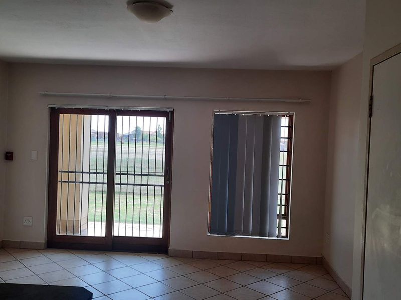 An empty living room featuring tiled flooring, a sliding glass door with security bars, and access to an outdoor area.