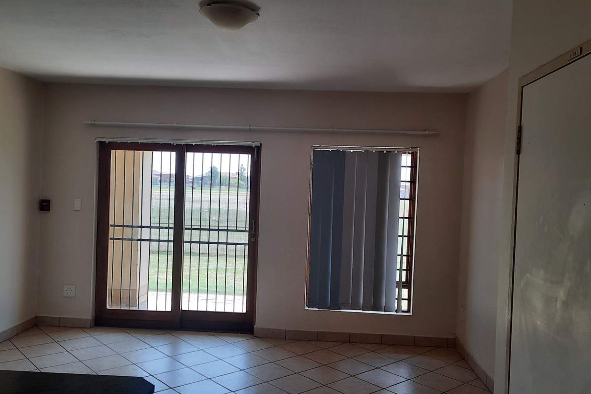 An empty living room featuring tiled flooring, a sliding glass door with security bars, and access to an outdoor area.
