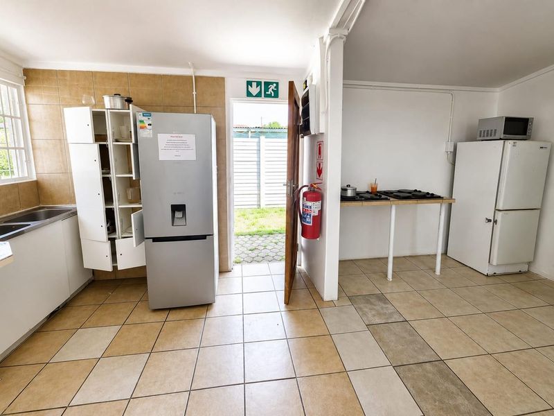 Functional kitchen area featuring tiled flooring, splashback, and direct access to the rear exterior. The space includes basic cabinetry and utility fixtures.