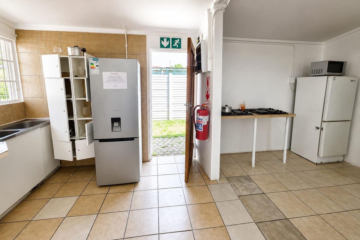 Functional kitchen area featuring tiled flooring, splashback, and direct access to the rear exterior. The space includes basic cabinetry and utility fixtures.