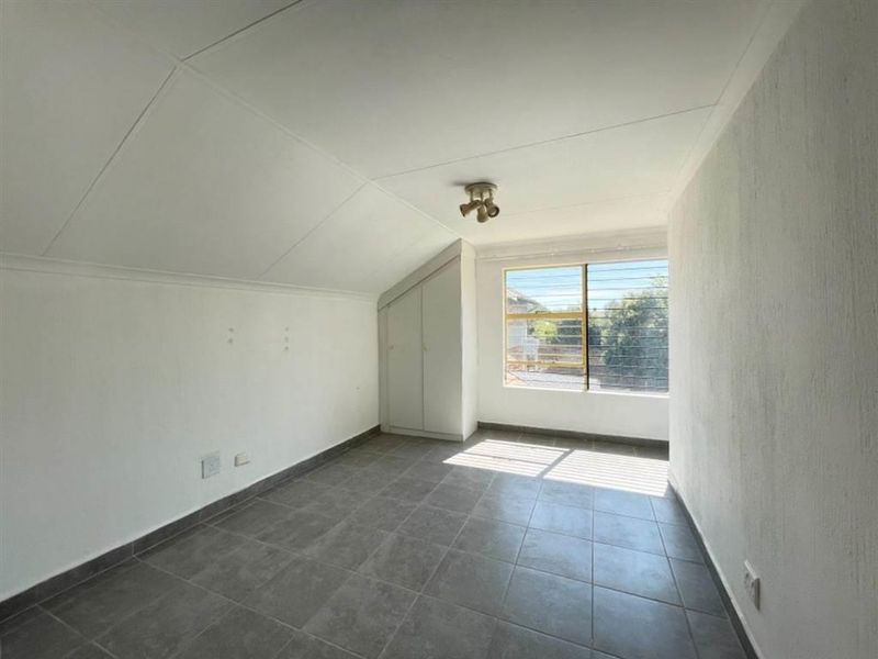 A vacant bedroom featuring tiled flooring, a sloped ceiling, and a built-in cupboard with security bars on the window.